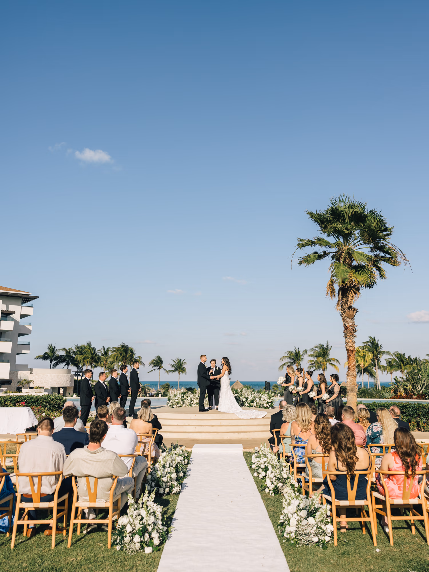A ceremony on a lawn above the Caribbean, guests seated under the palms