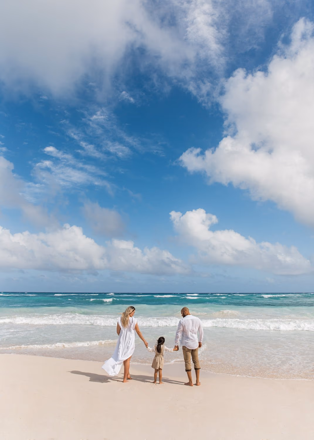 Family facing the water during a photoshoot in Tulum, with mom, dad, and daughter holding hands.