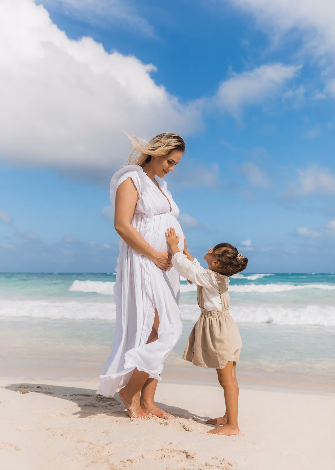 Mom showing her pregnant belly to daughter during a photoshoot on Tulum beach.